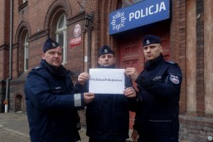 Zdjęcie przedstawia umundurowych policjantów. W tle znajduje się budynek KMP w Olsztynie.