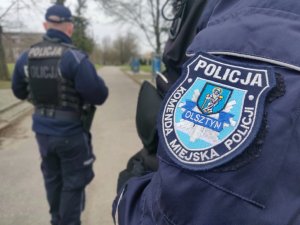 Zdjęcie przedstawia naszywkę KMP Olsztyn a w tle policjanta.