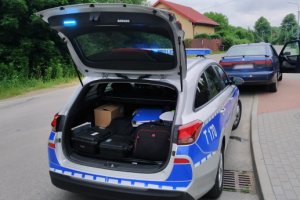 Zdjęcie przedstawia policyjny radiowóz a w tle samochód marki seat