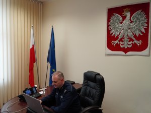 Zdjęcie przedstawia mł. insp. Roberta Zalewskiego siedzące przy  biurku przed laptopem.