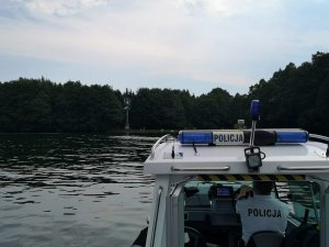 Zdjęcie przedstawia  fragment policyjnej łodzi na jeziorze a w tle maszt pogodowy.