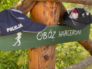 Zdjęcie przedstawia napis- obóz harcerski i czapkę z napisem policja.