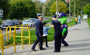 Zdjęcie przedstawia osoby przechodzące przez oznakowane przejście dla pieszych, na chodniku stoi policjant ruchu drogowego, a obok policjanta rozdająca odblaski.