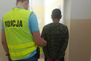 Zdjęcie przedstawia policjanta, który prowadzi zatrzymanego.