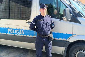 Zdjęcie przedstawia umundurowanego policjanta, w tle radiowóz.