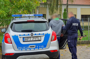 Zdjęcie przedstawia policjanta, który prowadzi zatrzymanego mężczyznę.