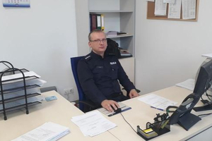 Zdjęcie przedstawia umundurowanego policjanta siedzącego przy biurku.