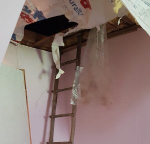 Zdjęcie przedstawia zdemolowany pokój, dziurę w suficie, drewnianą drabinę.