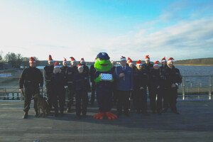 Zdjęcie przedstawia policjantów, którzy składają życzenia świąteczne. W tle znajduje się jezioro.