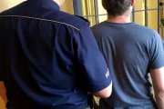 Zdjęcie przedstawia zatrzymanego mężczyznę prowadzonego przez umundurowanego policjanta.
