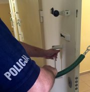 Zdjęcie przedstawia policjanta zamykającego policyjną kratę.