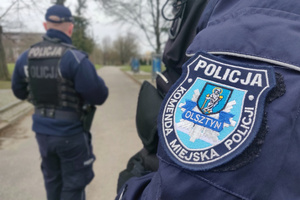 Zdjęcie przedstawia naszywkę KMP Olsztyn a w tle umundurowany policjant.