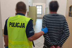 Zdjęcie przedstawia policjanta, który prowadzi zatrzymanego mężczyznę.