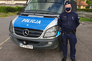 Zdjęcie przedstawia policjanta na tle radiowozu.