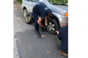 Zdjęcie przedstawia policjanta, który naprawia usterkę w aucie.