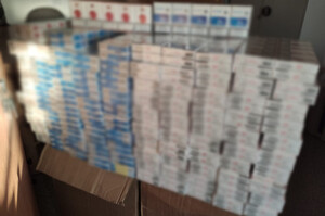 Zdjęcie przedstawia blisko tysiąc paczek papierosów bez polskich znaków akcyzy zabezpieczonych przez policjantów. Papierosy leżą na stole w pokoju.