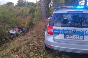 Zdjęcie przedstawia miejsce wypadku w pobliżu miejscowości Głotowo. Na pierwszym planie znajduje się fragment policyjnego radiowozu. W tle w przydrożnym rowie znajduje się uszkodzone auto koloru czerwonego.