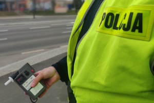 Zdjęcie przedstawia fragment umundurowanego policjanta, który trzyma w ręku urządzenie do badania stanu trzeźwości.