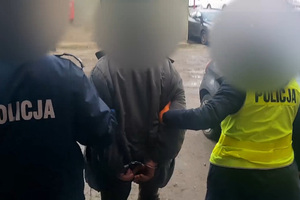 Zdjęcie przedstawia policjantów prowadzących zatrzymanego mężczyznę.