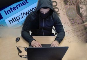 Zdjęcie przedstawia zamaskowanego mężczyznę siedzącego przy laptopie. Po lewej stronie adres www, po prawej pieniądze.