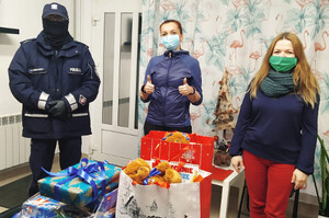 Zdjęcie przedstawia zapakowane prezenty na stole m.in. klocki, brązowe pluszowe misie oraz torebki koloru czerwonego i białego. Na pierwszym planie umundurowany policjant i dwie kobiety.