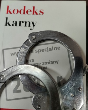 Zdjęcie przedstawia fragment kodeku karnego oraz policyjne kajdanki.