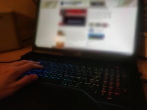 Zdjęcie przedstawia fragment laptopa i męską rękę.
