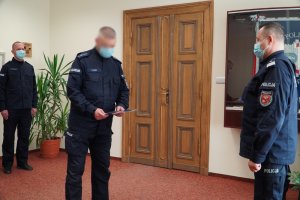 Wyróżnienie policjantów z Komendy Miejskiej Policji w Olsztynie. Zdjęcie przedstawia wyróżnionych policjantów w obecności nadinsp. Tomasza Klimka - szefa warmińsko-mazurskiej Policji. Funkcjonariusze są w umundurowaniu ćwiczebnym a na twarzach mają maseczki ochronne również koloru niebieskiego.