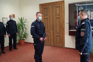 Wyróżnienie policjantów z Komendy Miejskiej Policji w Olsztynie. Zdjęcie przedstawia wyróżnionych policjantów w obecności nadinsp. Tomasza Klimka - szefa warmińsko-mazurskiej Policji. Funkcjonariusze są w umundurowaniu ćwiczebnym a na twarzach mają maseczki ochronne również koloru niebieskiego.