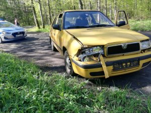 Na zdjęciu widoczny samochód osobowy m-ki Skoda Felicia koloru żółtego. Auto stoi przodem, ma rozbity prawy przedni reflektor. Za pojazdem w odległości kilku metrów znajduje się policyjny radiowóz.