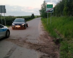 Zdjęcie przedstawia miejsce zdarzenia drogowego w m. Godki. Na pierwszym planie znajduje się osobowy ford a obok fragment policyjnego radiowozu.