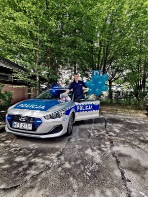 Zdjęcie przedstawia policjanta z Posterunku Policji I w Olsztynie, który w związku Dnia Dziecka przekazuje najmłodszym niebieskie balony oraz lizaki.