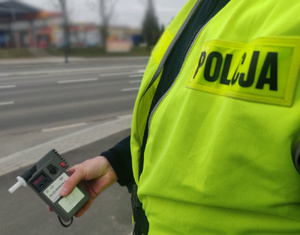 Zdjęcie przedstawia fragment policjanta trzymający w ręku alkomat.