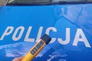 Zdjęcie przedstawia fragment policyjnego radiowozu oraz urządzenie do badania stanu trzeźwości.