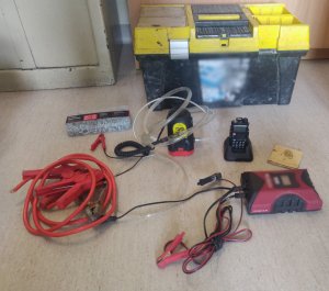 Zdjęcie przedstawia zabezpieczone przedmioty przez policjantów położone na podłodze m.in. czarno-żółta skrzynka na narzędzia, czerwone kable, elektronarzędzia.