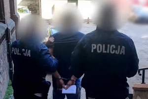Zdjęcie przedstawia policjantów prowadzących zatrzymanego mężczyznę.