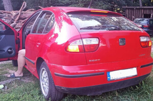 Zdjęcie predstawia auto koloru czerwonego. W tle posesja.