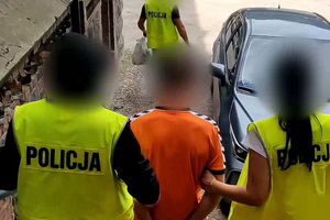 Zdjęcie przedstawia policjantów prowadzących zatrzymanego mężczyznę do auta.