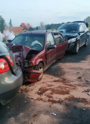 Fotografia przedstawia trzy samochody osobowe uszkodzone na skutek kolizji drogowej. Jezdnia, na której stoją auta pokryta jest sorbentem - pomarańczowy proszek rozsypany po jezdni w celu zneutralizowania skutków wycieku płynów eksploatacyjnych.