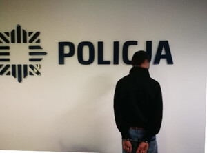 Zdjęcie przedstawia zatrzymanego mężczyznę w budynku. W tle napis "Policja".