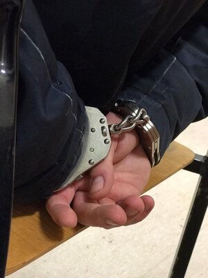 Zdjęcie przedstawia fragment mężczyzny siedzącego na krześle w kajdankach.