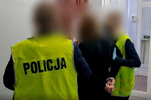 Zdjęcie przedstawia nieumundurowanych policjantów prowadzących zatrzymanego mężczyznę.