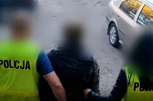 Zdjęcie przedstawia nieumundurowanych policjantów prowadzących zatrzymanego mężczyznę.