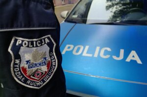 Zdjęcie przedstawia fragment policyjnego radiowozu oraz umundurowanego policjanta.