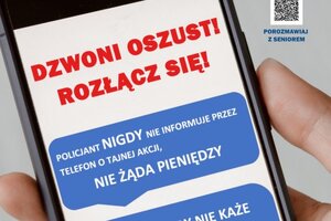 Na grafice znajduje się dłoń trzymająca smartfona, na którym wyświetlane jest hasło Dzwoni oszust! Rozłącz się!