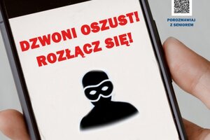 Na zdjęciu widoczna jest dłoń trzymająca telefon, na którym wyświetlany jest napis "Dzwoni oszust! Rozłącz się!" oraz sylwetka zamaskowanego przestępcy.