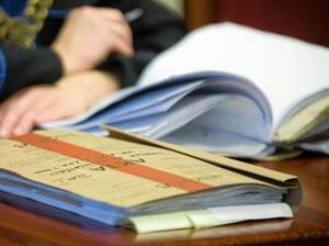 Zdjęcie przedstawia fragment tomu akt oraz w tle fragment sędziego.