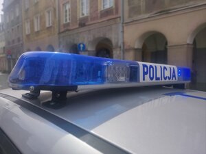 Zdjęcie przedstawia fragment radiowozu na tle budynku.