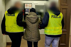 Zdjęcie przedstawia prowadzenie zatrzymanej kobiety przez dwóch policjantów.
