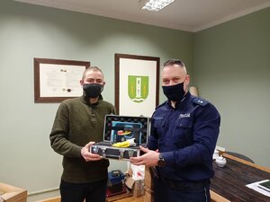 Zdjęcie przedstawia Wójta Gminy Świątki oraz Z-ce Komendanta Komisariatu Policji w Dobrym Mieście przekazujących sobie nowe alkomat w walizce w budynku Urzędu Gminy Świątki.